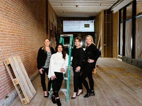 Four women standing together in a large room that is under construction